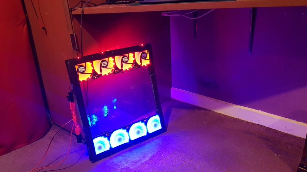 ck frame surrounds a plastic window. At the top of the window four red LED fans are glowing to blow warm air out, at the bottom of the window four blue fans suck air in. 